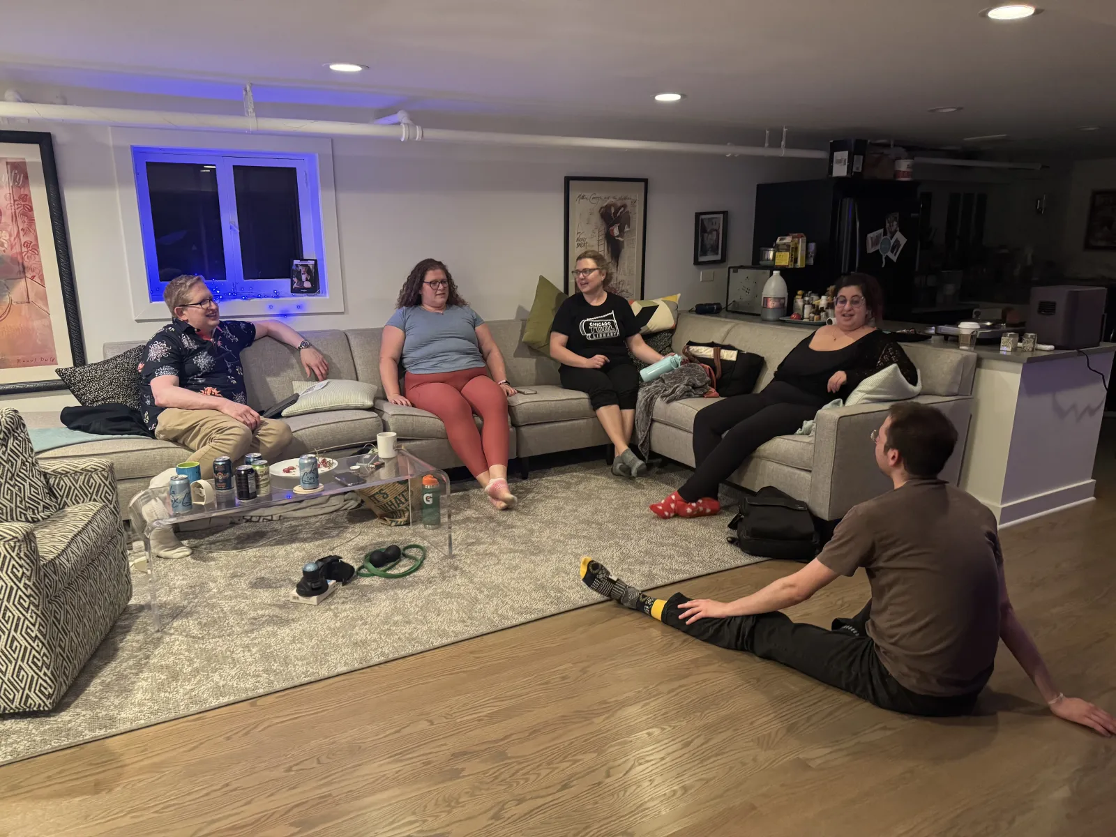 Friends sit together on a sofa and the floor during an evening get-together.